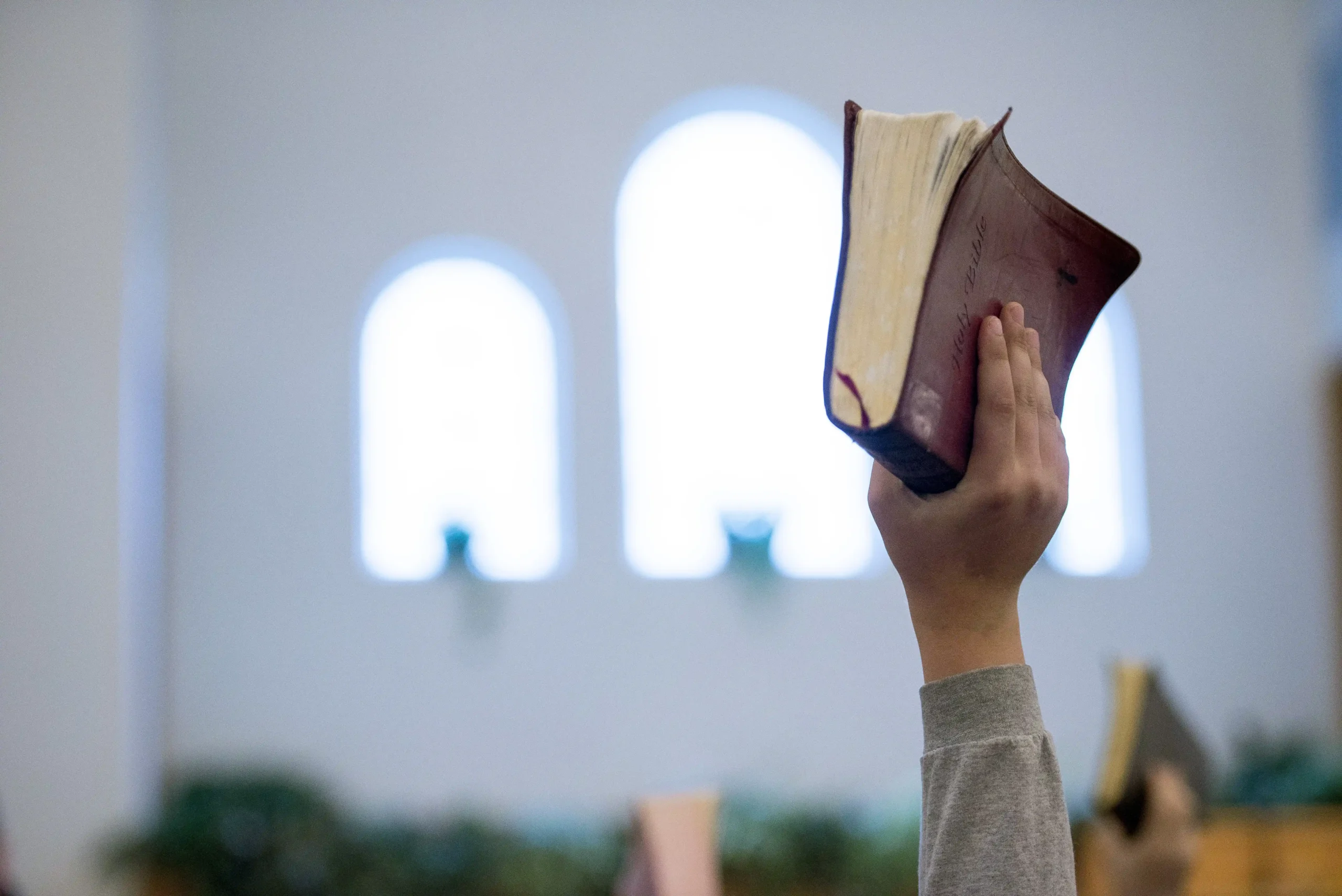 person holding up bible with blurred background
