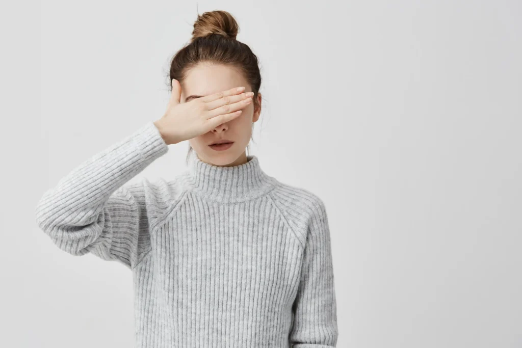 skinny woman wearing grey outfit closing her eyes with hand confident female trying hide her face from other people